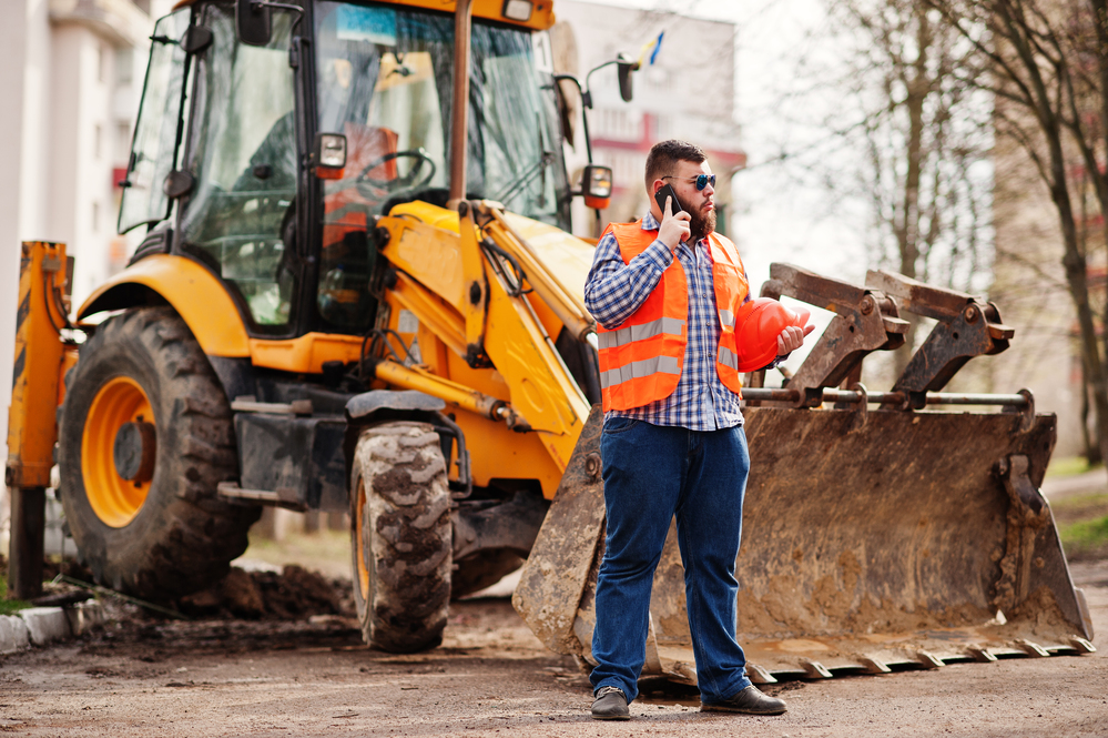 Construction equipment rental supervisor near yellow backhoe loader at job site in Azusa, CA