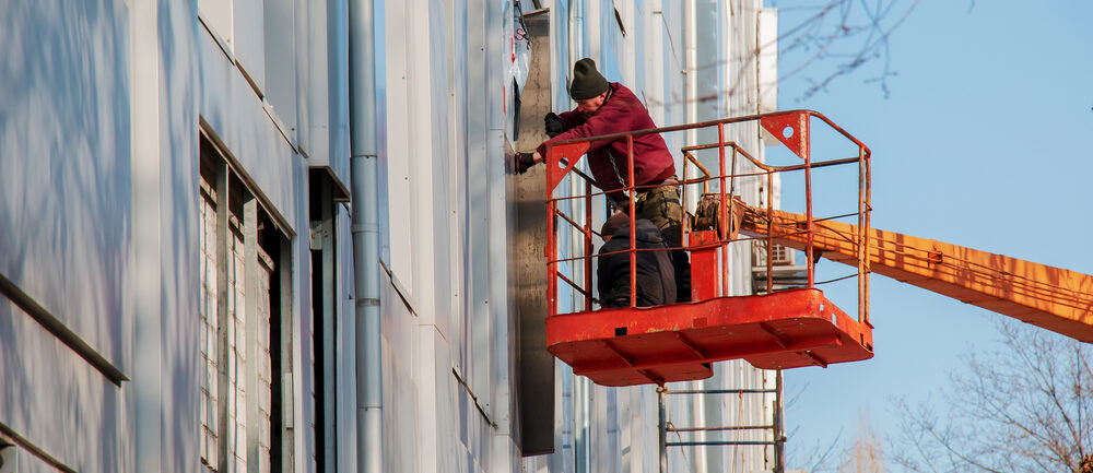 Worker using boom lift rental for exterior building maintenance in Richmond, California.