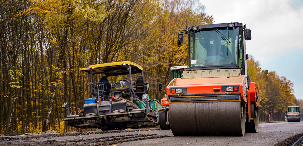 Asphalt rollers compacting a newly paved road through a wooded area in Collinsville, IL