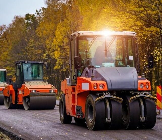 Asphalt rollers compacting a newly paved road through a wooded area in Dublin, CA