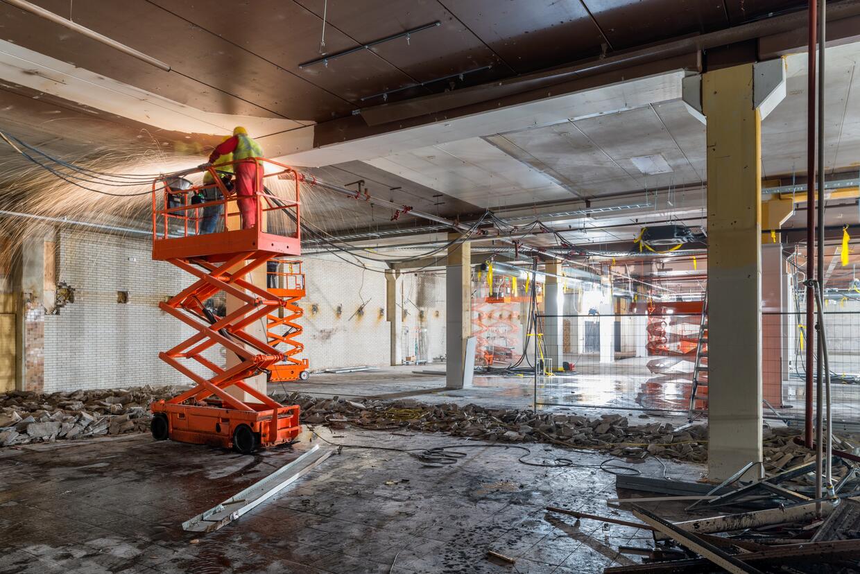 MANUAL WORKERS WELDING AT CONSTRUCTION SITE WHILE STANDING ON SCISSOR LIFT
