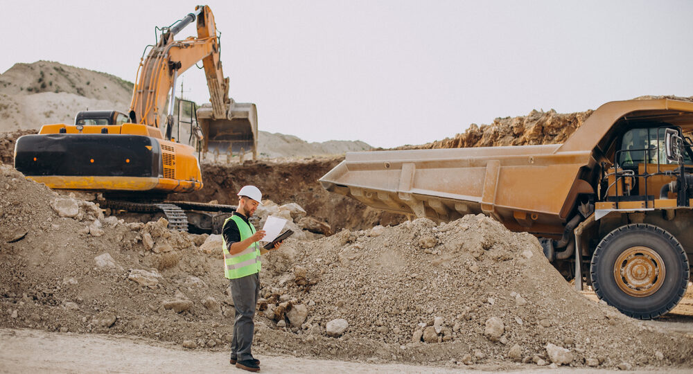 Excavator with visible boom, arm, and bucket loading soil into a dump truck